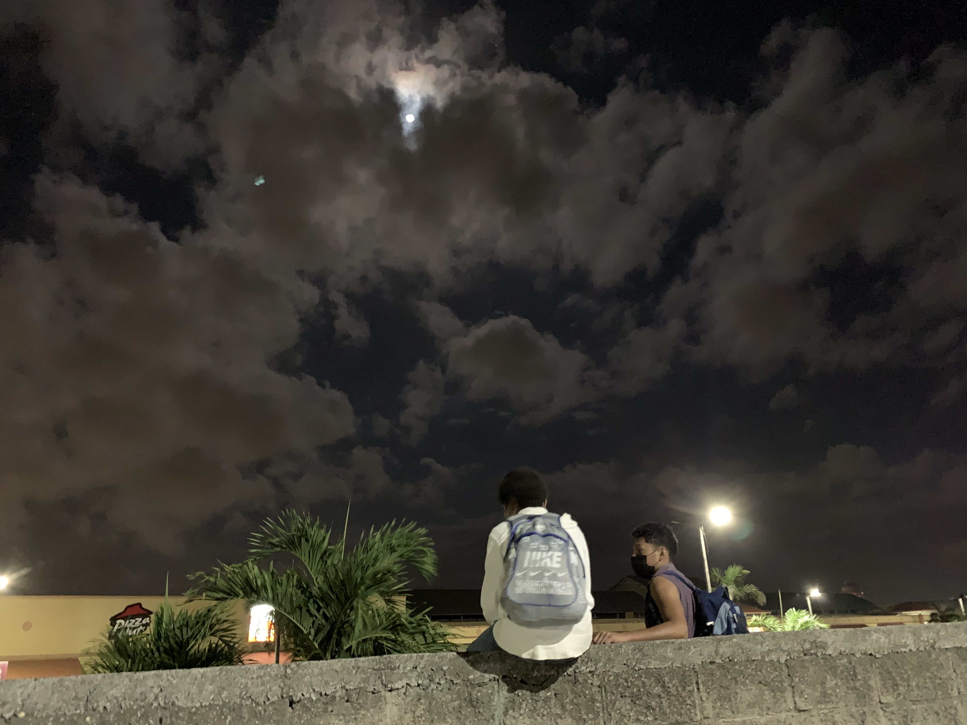 Jóvenes migrantes conversan sentados en el cerco que rodea la terminal de buses De San Pedro Sula. Foto: Dennis Arita