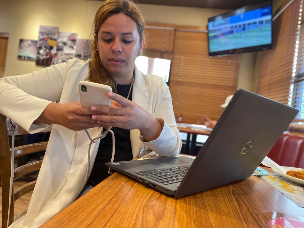 Lucía Valladares sentada trabajando con su computadora y celular en un restaurante